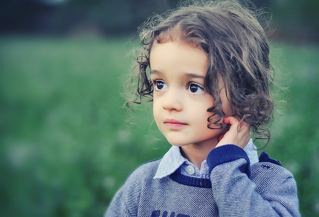 small brown haird girl with big eyes standing in a field touching here hair