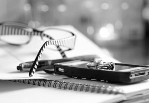 black and white photo of reading glasses, mobile phone and wedding rings sitting on top of a notebook on desk