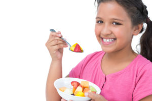 Smiling little girl eating fruit salad on white background