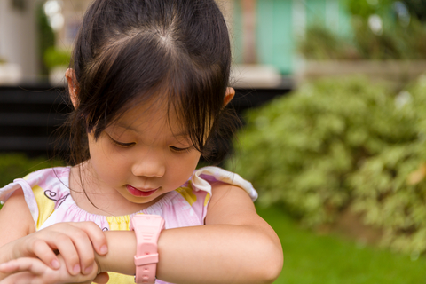 little asian child looking at her wrist watch outside