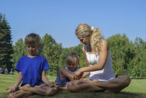 two children learning yoga in the park with their teacher