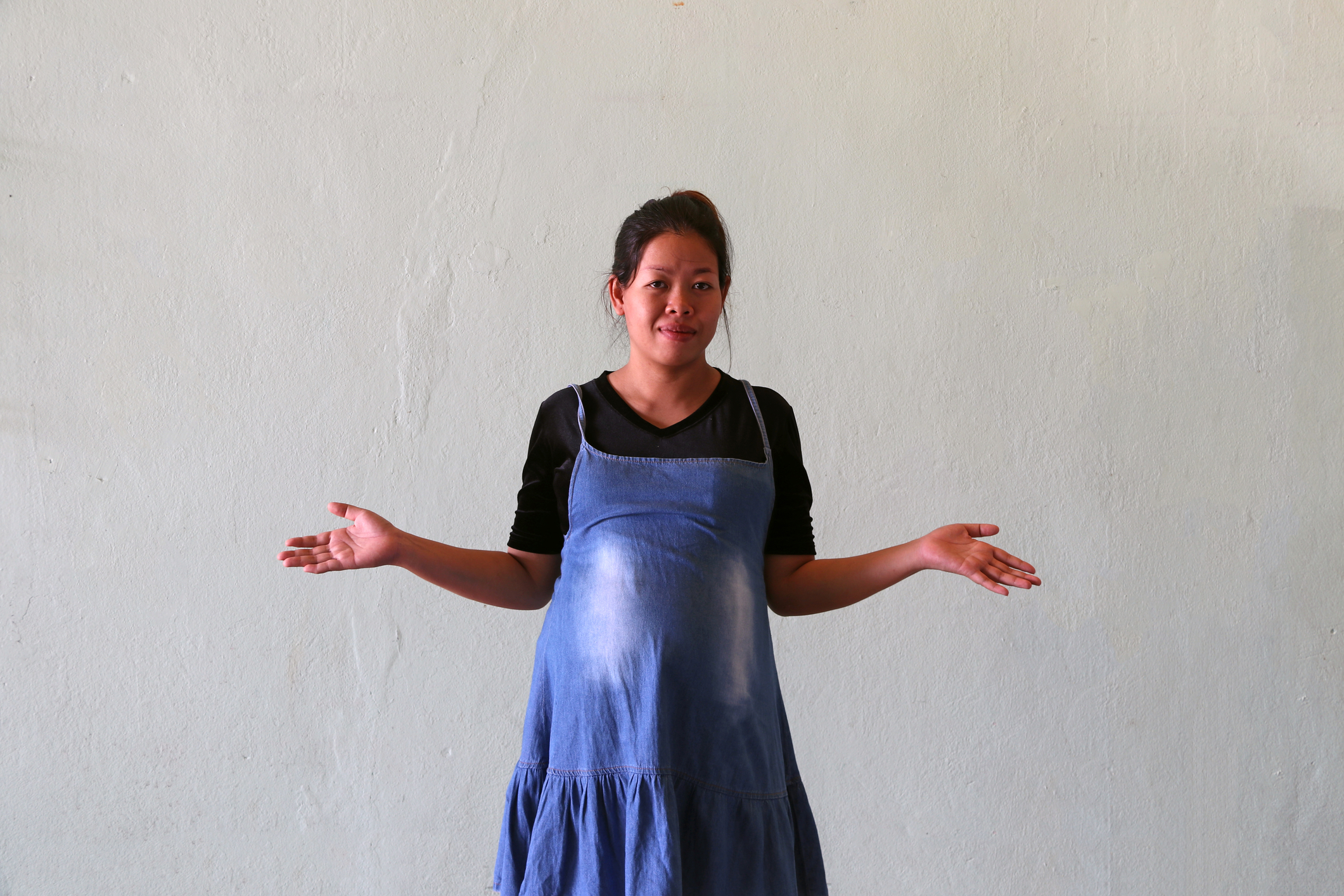 Pregnant woman use a denim skirt or jeans maternity clothes with black T-shirt, standing and waved both hands to the side of the body.