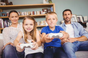 Smiling siblings playing video games with parents at home