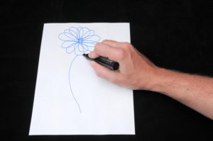 Male hand drawing picture of blue flower on white pad of paper for pictionary game
