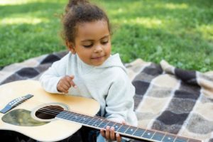 little girl sitting on a blanket on the grass, holding a guitar