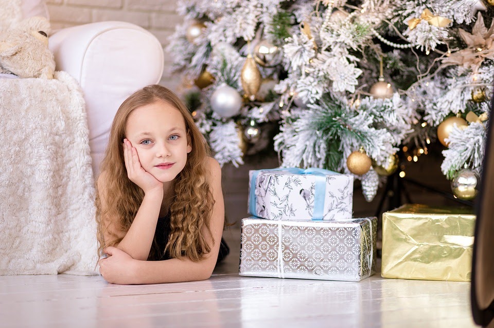 young girl laying on her stoacn on the living room floor beside a white Christmas tree and presents