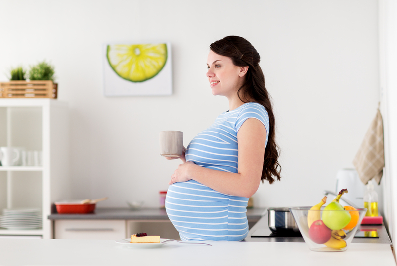 pregnant woman smiling while holding her belly and drinking tea