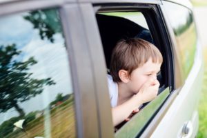 Seven years old small child in the backseat of a car sitting in children safety car seat covers his mouth with his hand