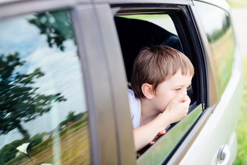Seven years old small child in the backseat of a car sitting in children safety car seat covers his mouth with his hand