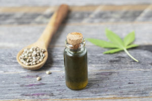 Small bottle of CBD oil with cannabis leaf and seeds in a wooden spoon