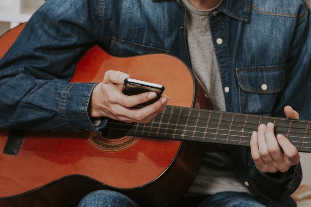 man holding guitar while looking at his phone