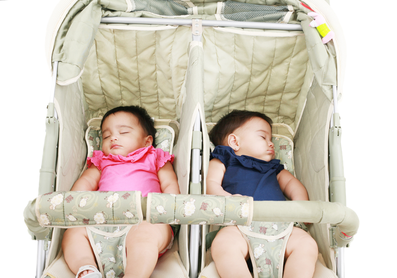 black haired twins sleeping in double stroller on white back ground
