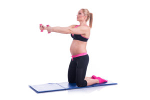 pregnant woman exercising with weights kneeling on mat on white background
