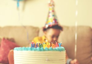 african toddler wearing party hat sitting in front of birthday cake