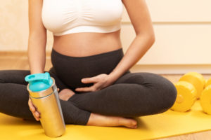 pregnant women sitting on yoga mat holding protein shake